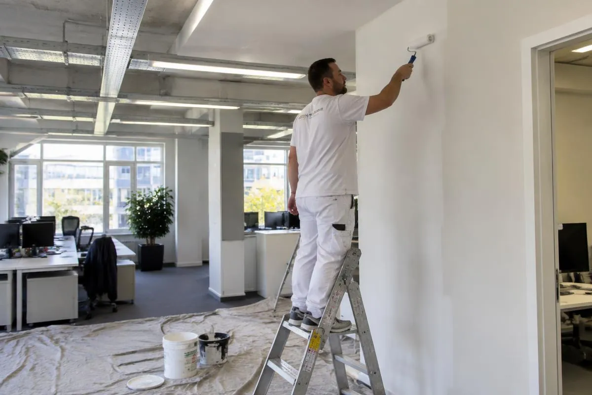 Painter rolling fresh white paint in an open-plan office with protected floors